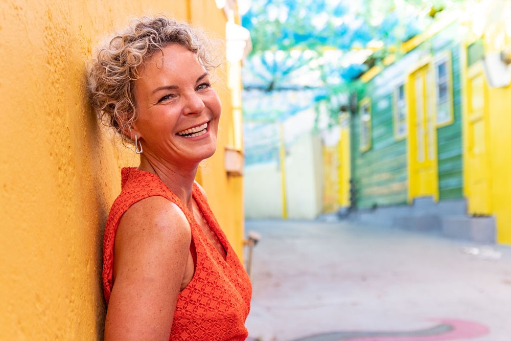 Daisy Kuipers, marketingstrateeg voor de kinderopvang en auteur van LEF in de kinderopvang!, lachend tegen een gele muur